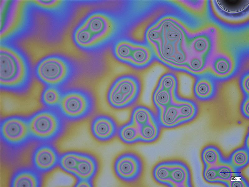 microscope image of collected aerosol particles; they appear like an oil-on-water effect, with swirls of muted colors